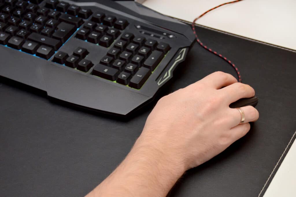 Guy is playing a video game. Close up of a hand lying on a mouse and a black gaming keyboard on a black table. Top view