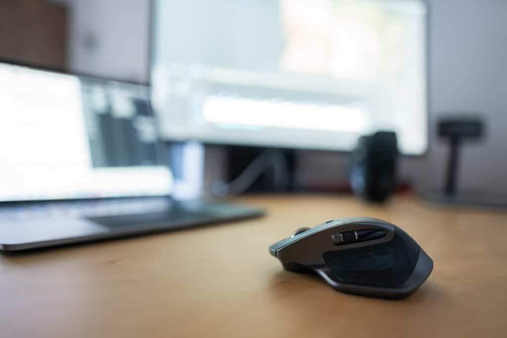 Closeup of a gaming mouse with a blurred laptop and a monitor in the background